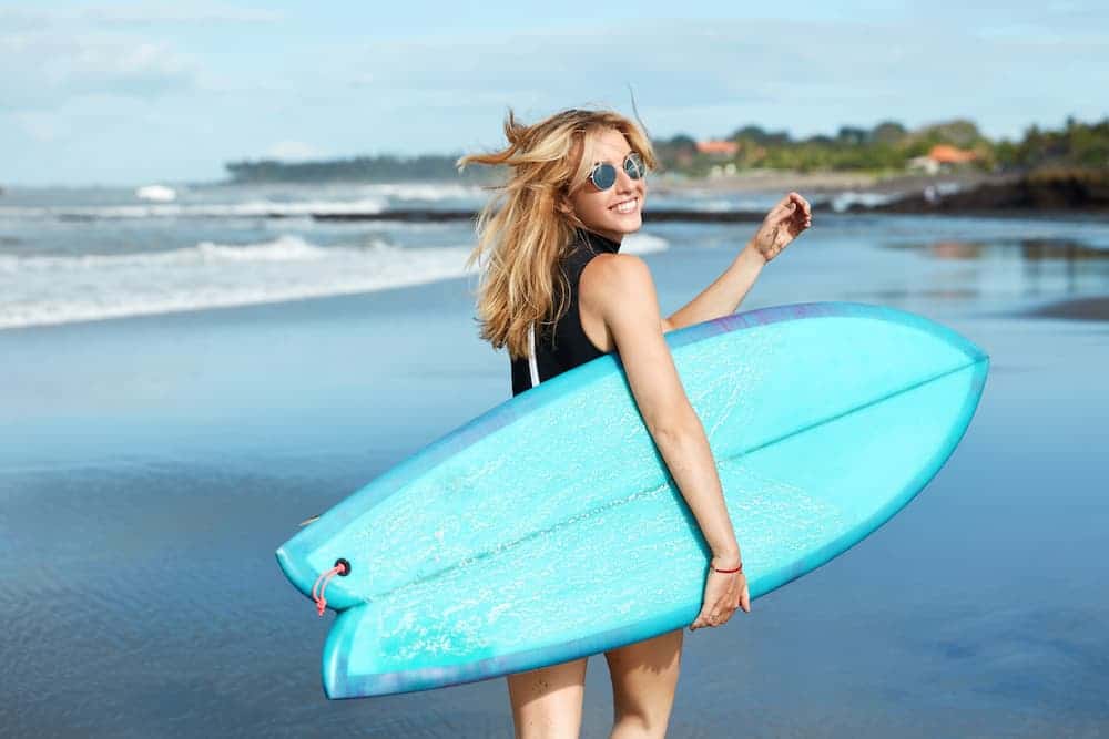 woman holding surfboard at the beach smiling 