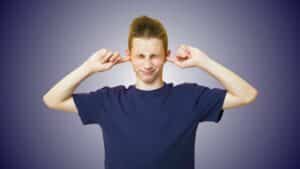 Teen boy pressing fingers in ears due to discomfort, symbolising ear wax issues