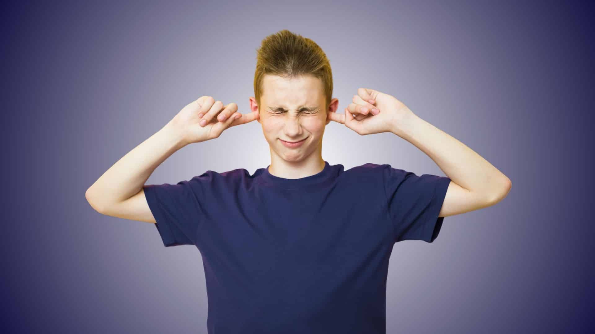 Teen boy pressing fingers in ears due to discomfort, symbolising ear wax issues