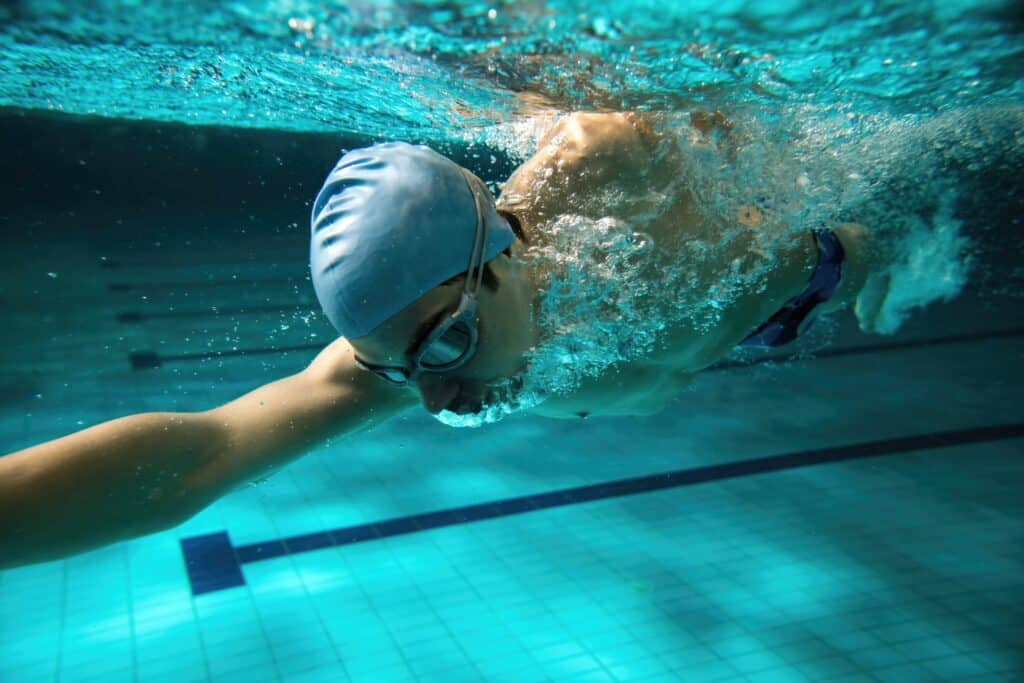 Swimmer underwater in pool wearing swim cap and goggles, potential ear health concern